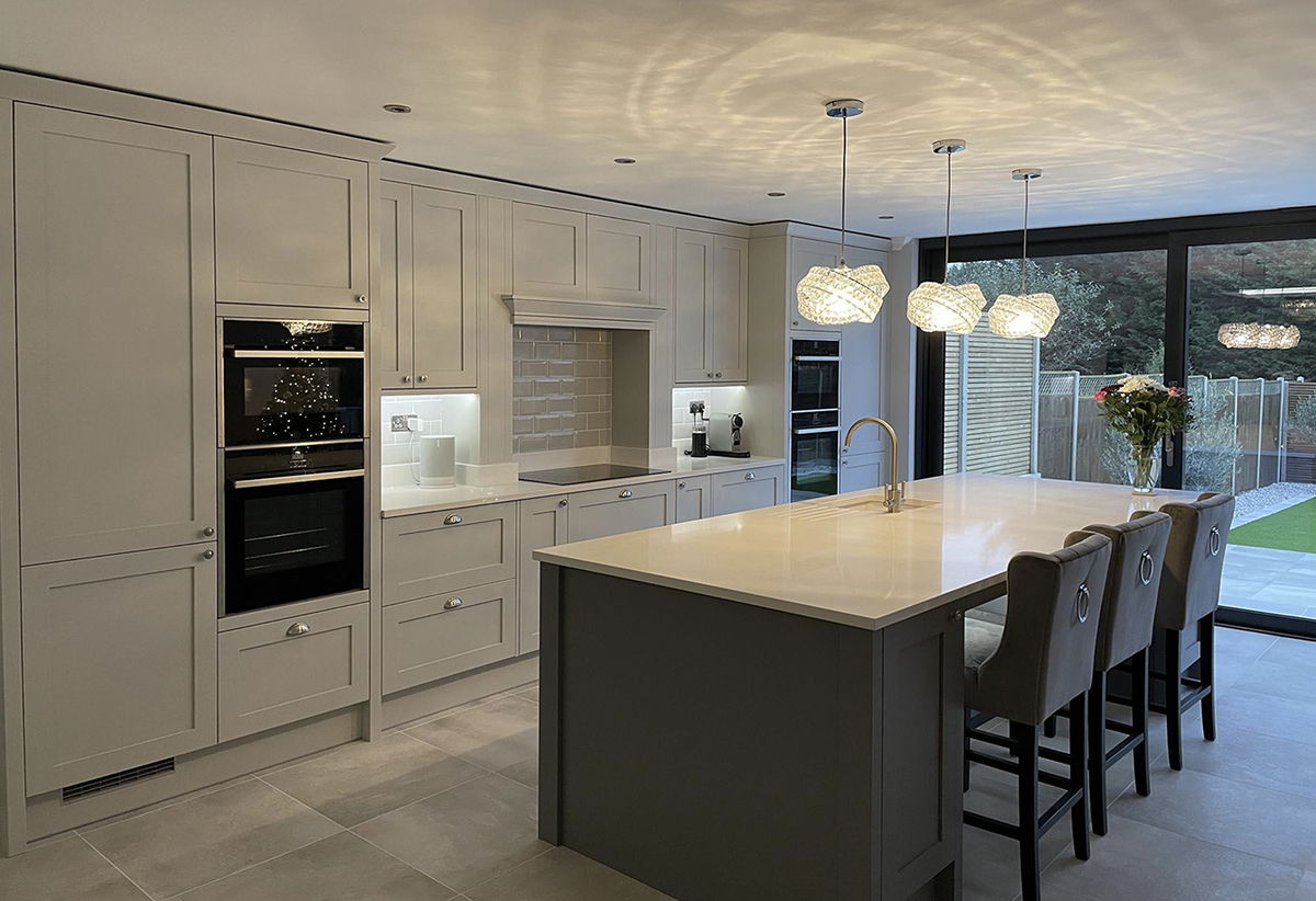 A shaker kitchen with a large island and breakfast stools inside a completed chalet conversion, opening onto the garden through full width glazing