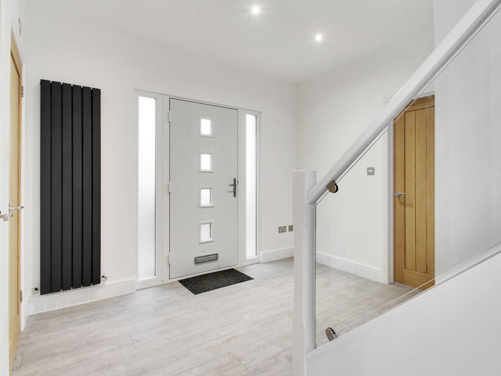 The hallway of a completed chalet conversion, with a new staircase and glass balustrade rising to the full height first floor