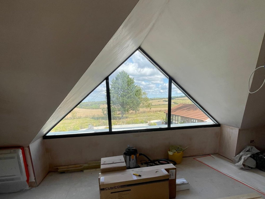 The converted loft plastered out, with the triangular gable window installed and the view over open fields through it, by LD&C Homes