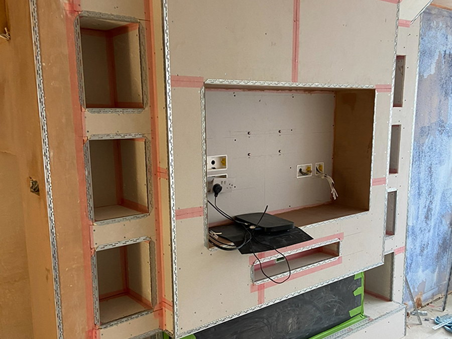 The media wall under construction, boarded and taped out with recessed shelving and openings formed for the screen and the fire, by LD&C Homes