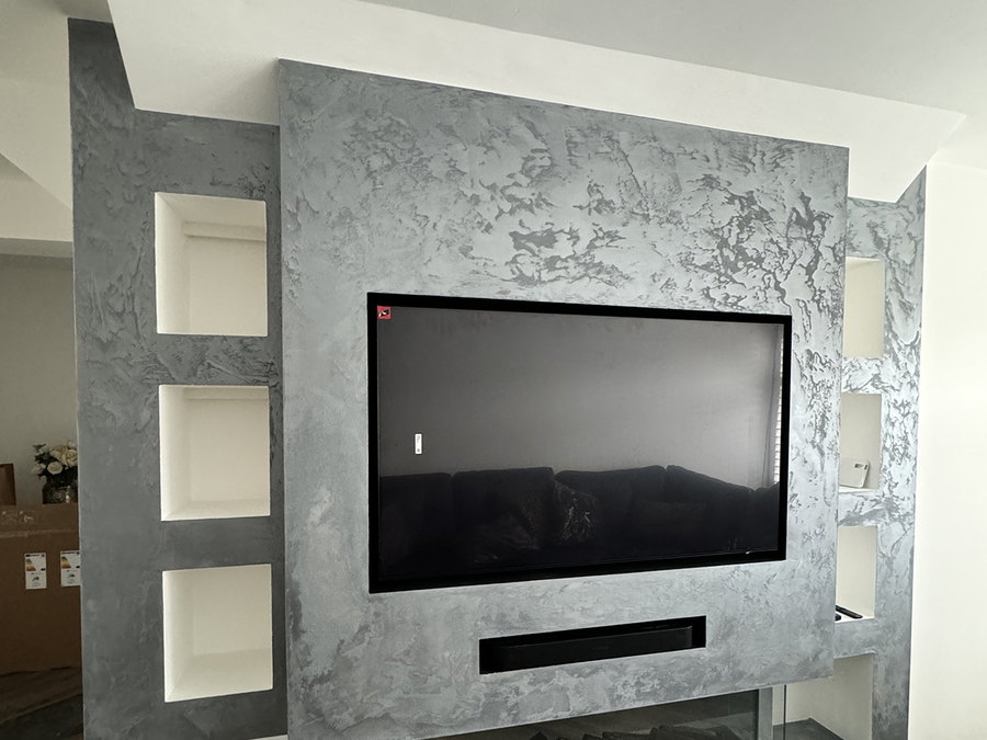 The finished media wall in polished plaster, with recessed shelving, a mounted screen and a long inset fire below, by LD&C Homes