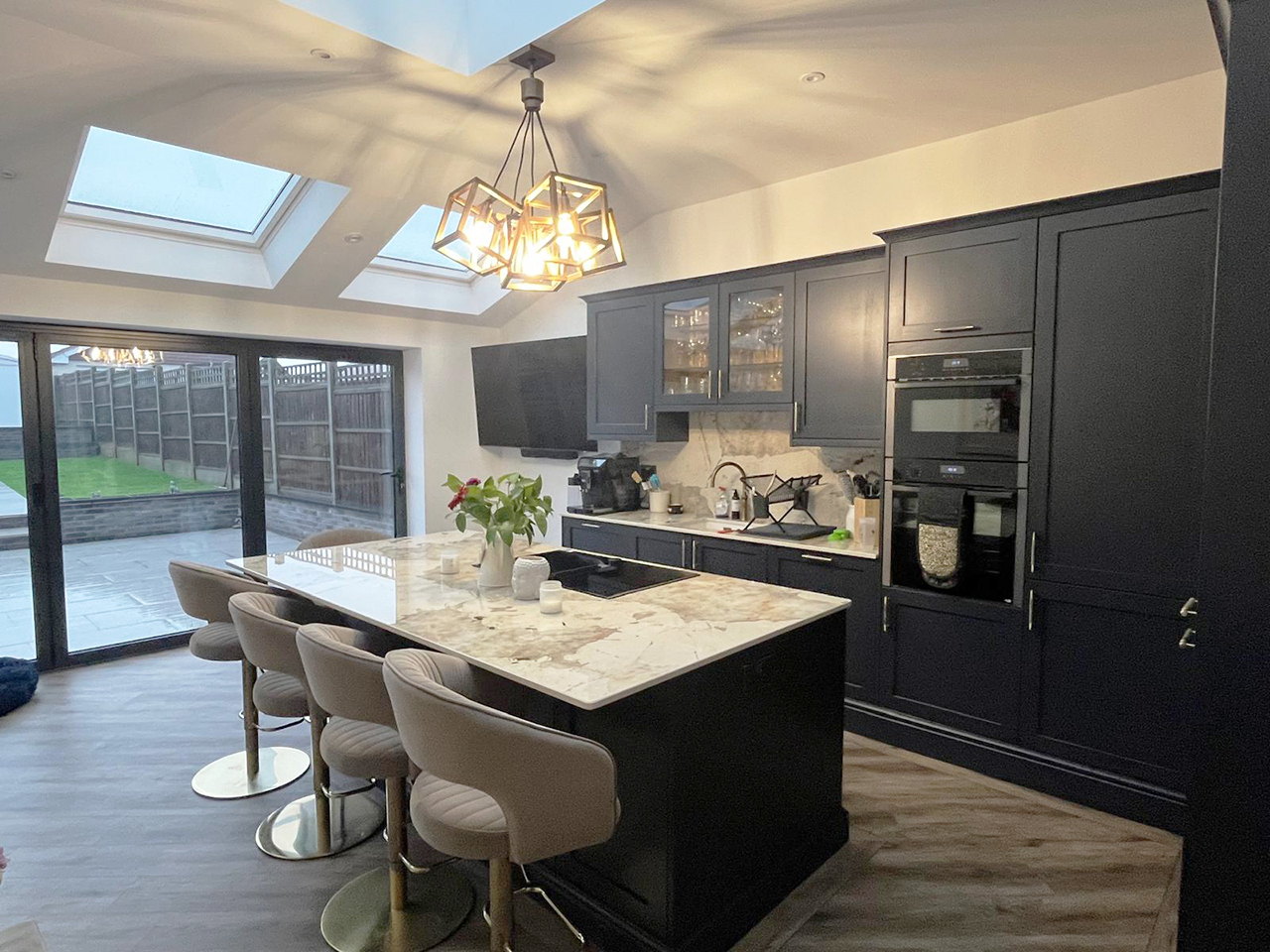 The finished open plan kitchen in a single storey rear extension, with a marble island, dark shaker units, three roof windows and bifold doors onto the garden, built by LD&C Homes