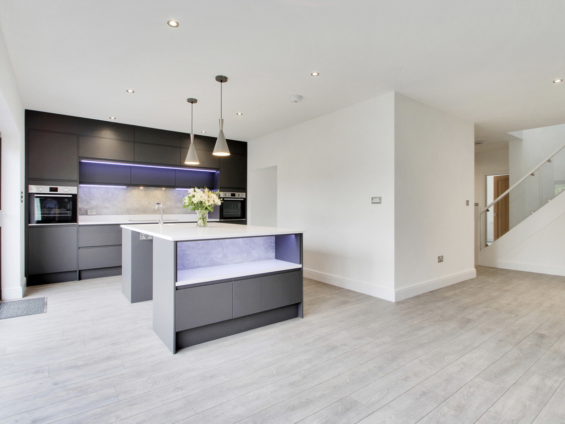 A newly finished open plan kitchen extension with dark handleless units, an island with an integrated worktop and sliding doors along one wall, built by LD&C Homes