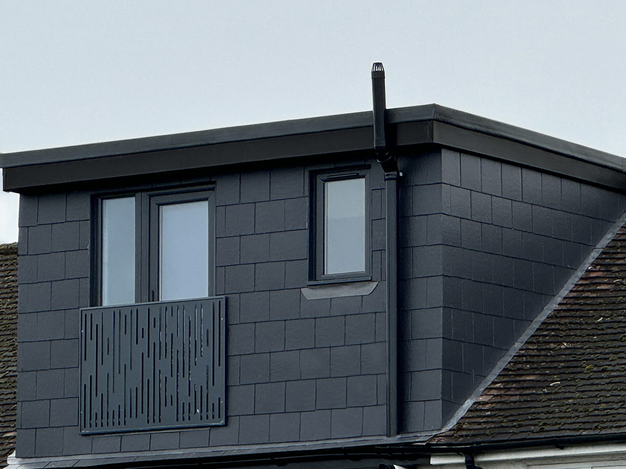A slate clad flat roof dormer loft conversion with dark framed windows and a Juliet balcony, built by LD&C Homes