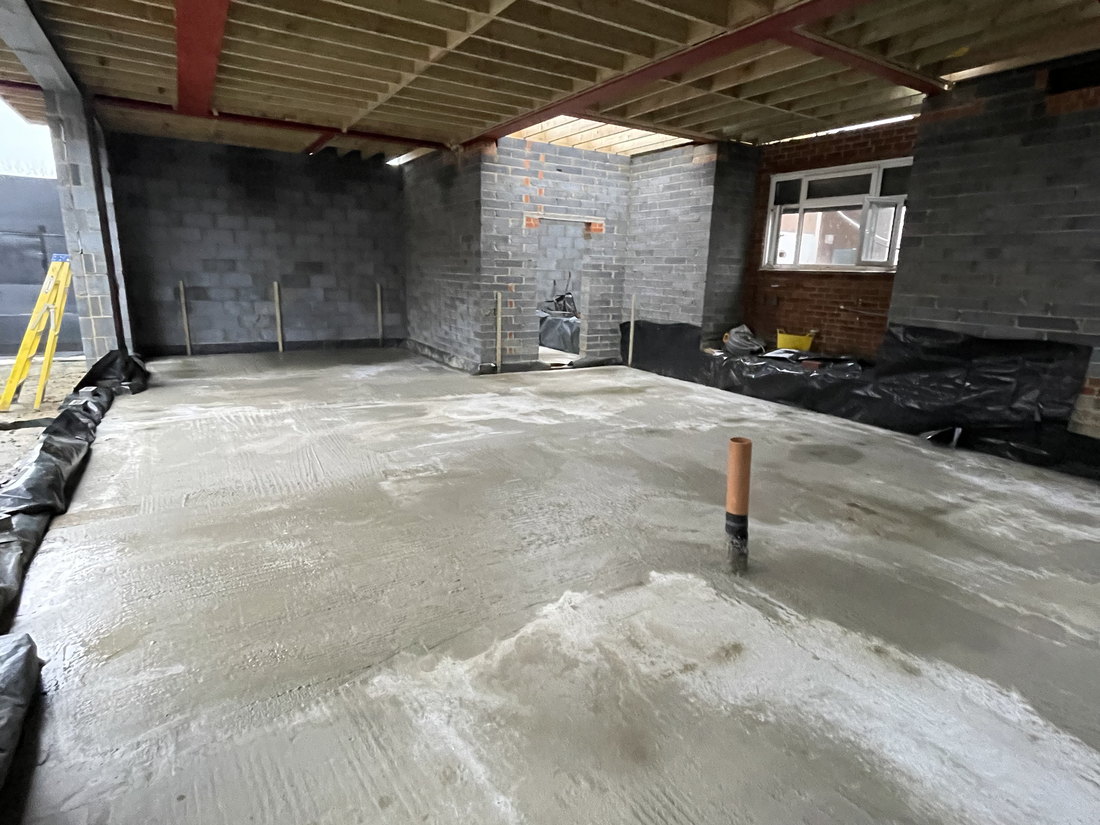 The ground floor as a shell, with the new slab poured, blockwork walls and the steel structure overhead before first fix, by LD&C Homes
