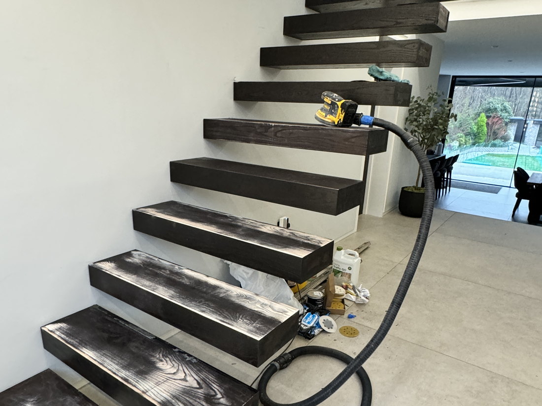 The floating staircase treads being sanded and finished on site, cantilevered from the wall with no visible support, by LD&C Homes