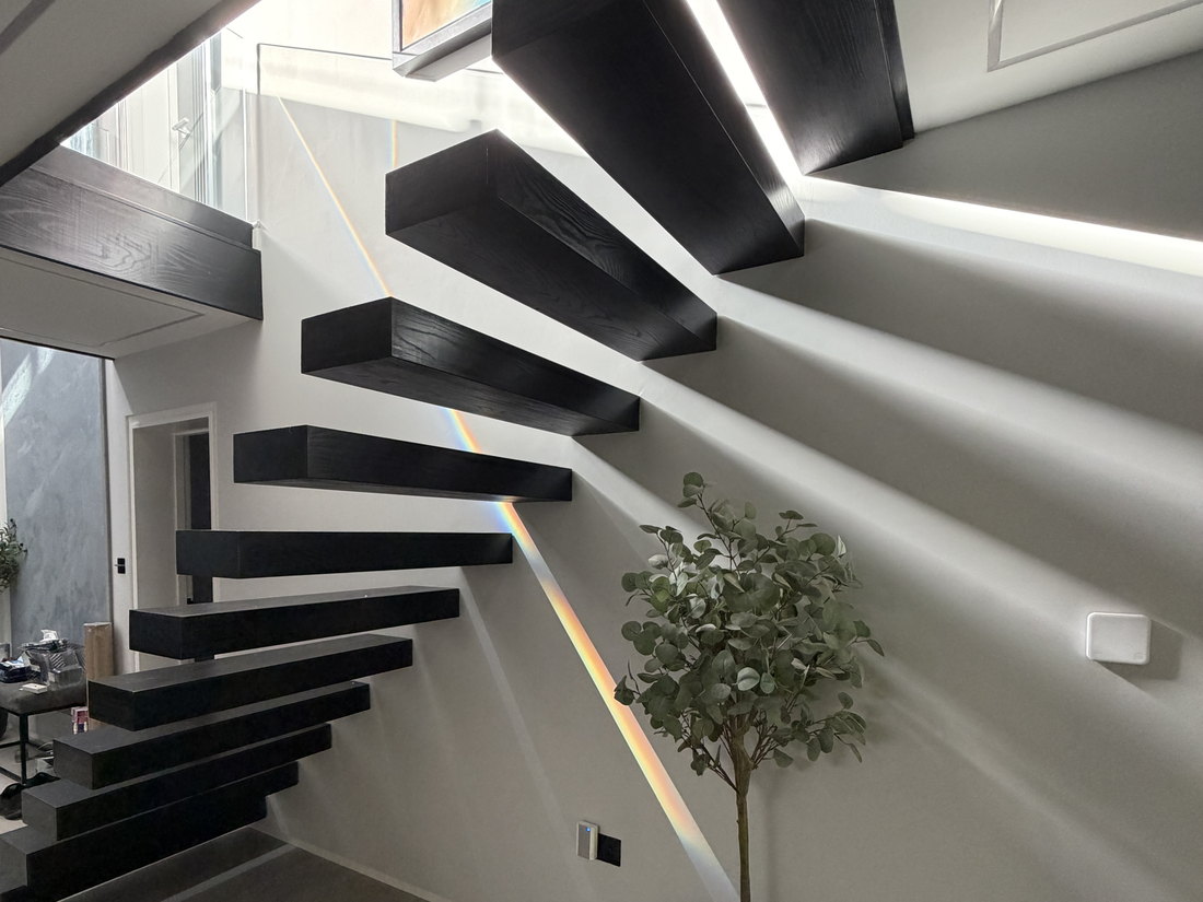The finished floating staircase seen from below, showing the cantilevered treads, the concealed lighting behind them and the gallery landing above, by LD&C Homes