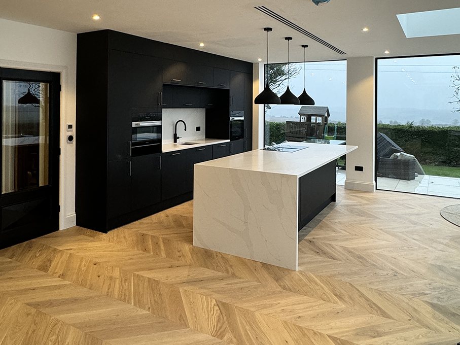 Open plan kitchen with black units, a marble island and a herringbone oak floor in a rear extension in Eynsford, Kent